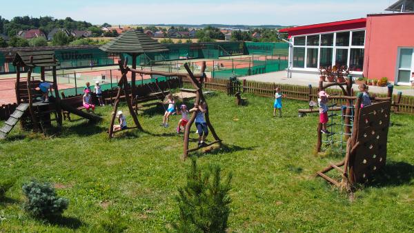 Dětské hřiště u klubovny s prolézačkami, v pozadí kurty