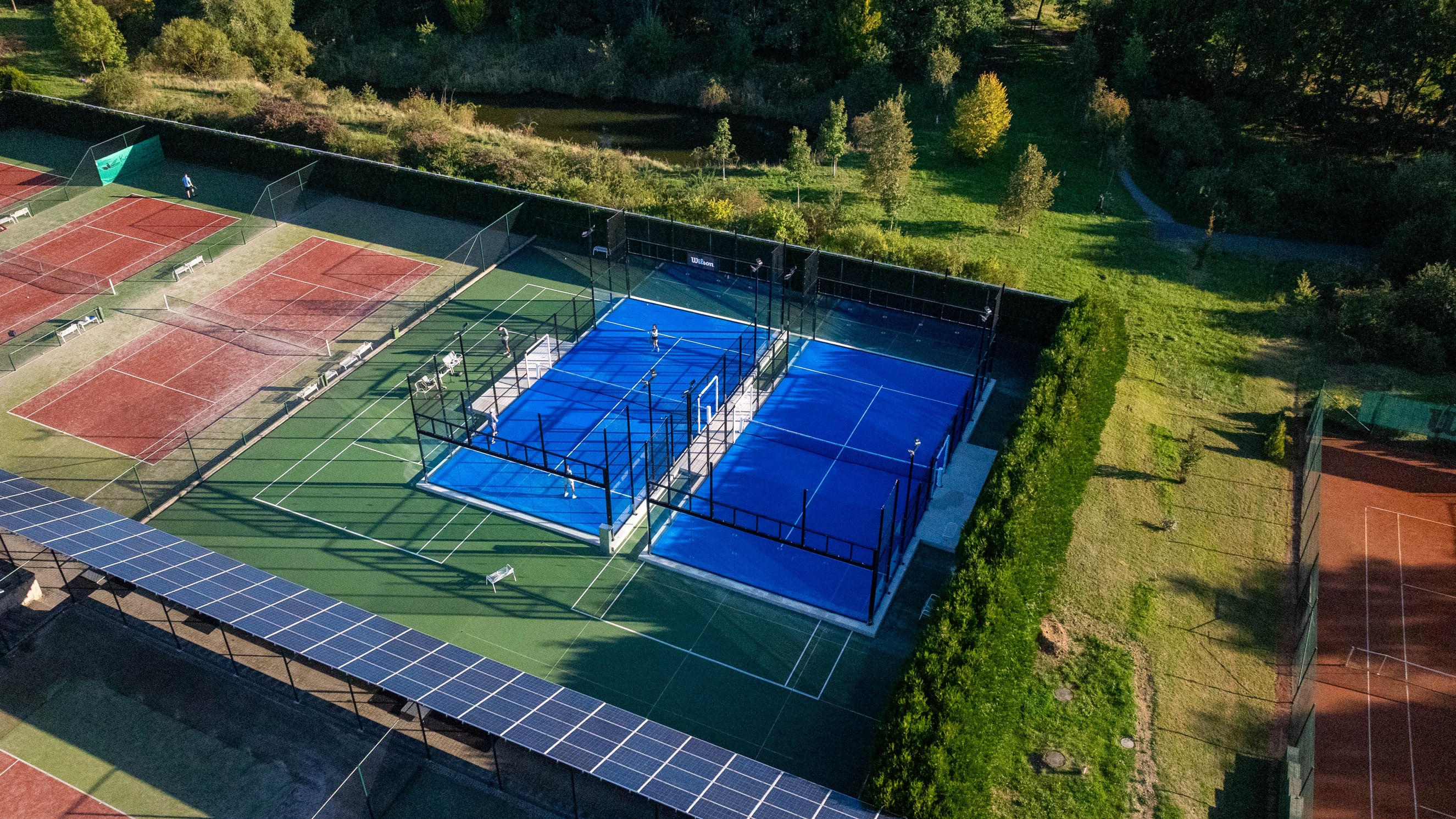 Padelové kurty areálu Wilson, v pozadí venkovní tenisové kurty a zeleň